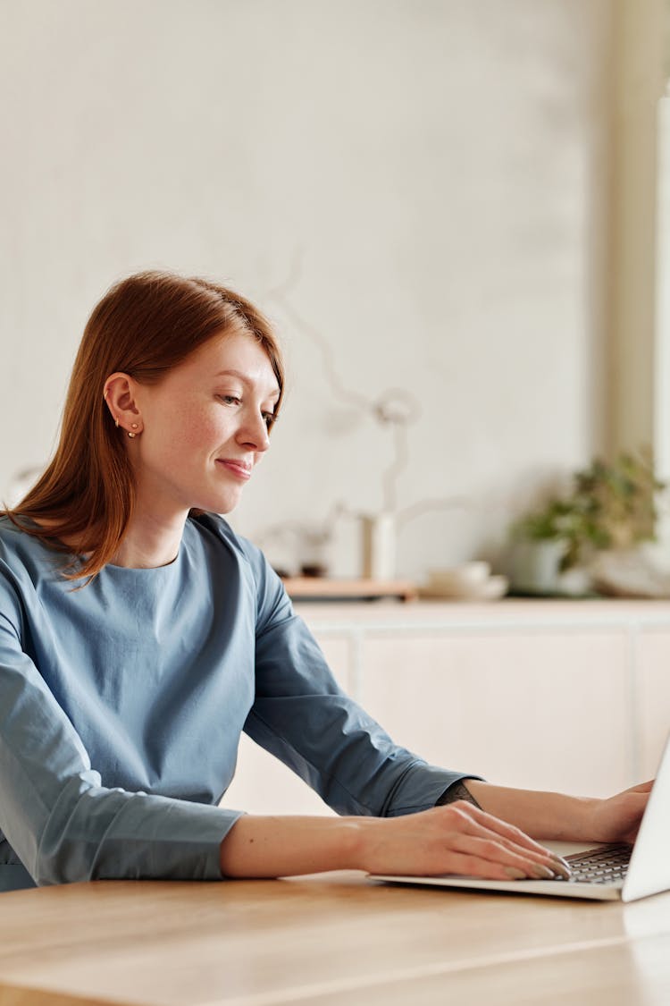 Woman In Blue Long Sleeves Using A Laptop While Sitting On The Table 