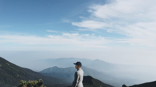 Unrecognizable tourist contemplating mountains on foggy day under cloudy sky