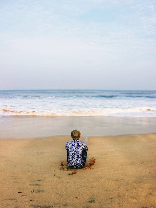 Unrecognizable traveler resting on sandy coast near ocean under sky