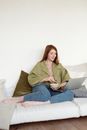 一位穿着绿色西装外套、拿着笔记本电脑的女人，在室内带枕头的沙发上放松身心