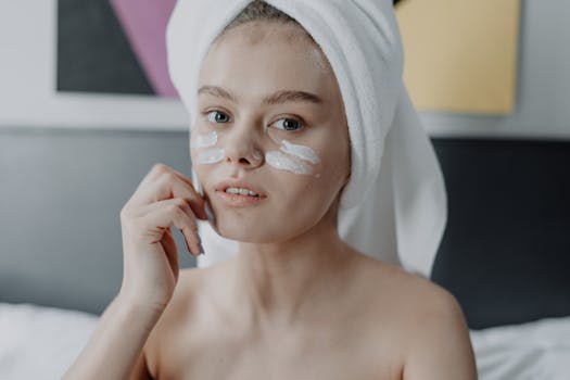 A young woman with facial cream and a towel wrapped on her head, focused on skincare.