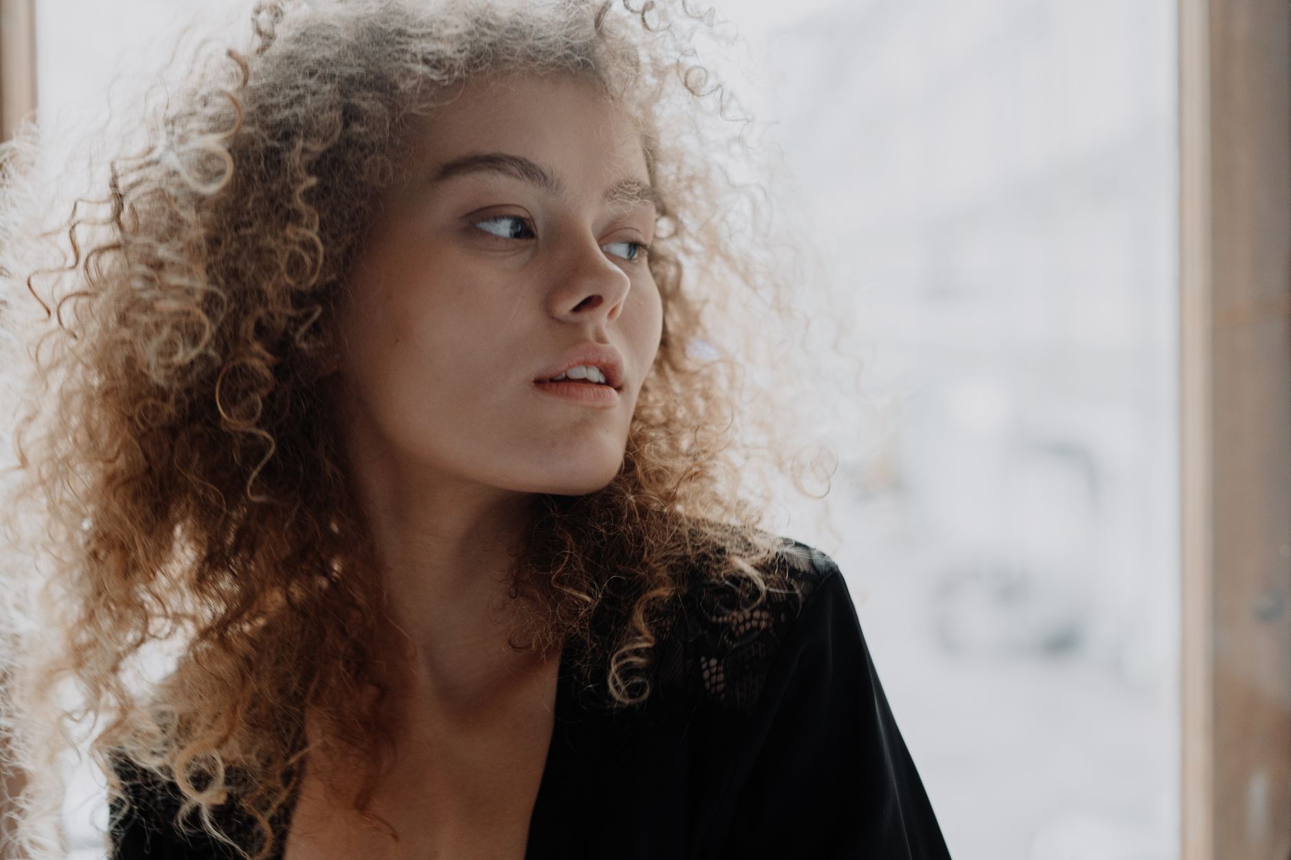 Natural light portrait of a young woman with curly hair, exuding elegance and beauty.