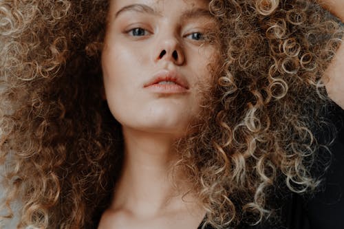 Close-up portrait of a young woman with natural curly hair and minimal makeup.