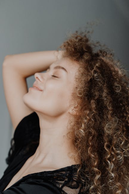 A serene side profile portrait of a young woman with curly hair, eyes closed, in a relaxed pose.