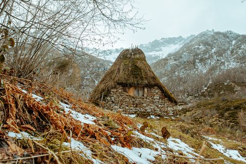 Free Old stone hut with thatched roof and small window located between mountains in highland on overcast winter day Stock Photo