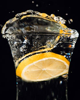 Close-up of a lemon slice splashing into water with a dramatic splash effect on a black background.