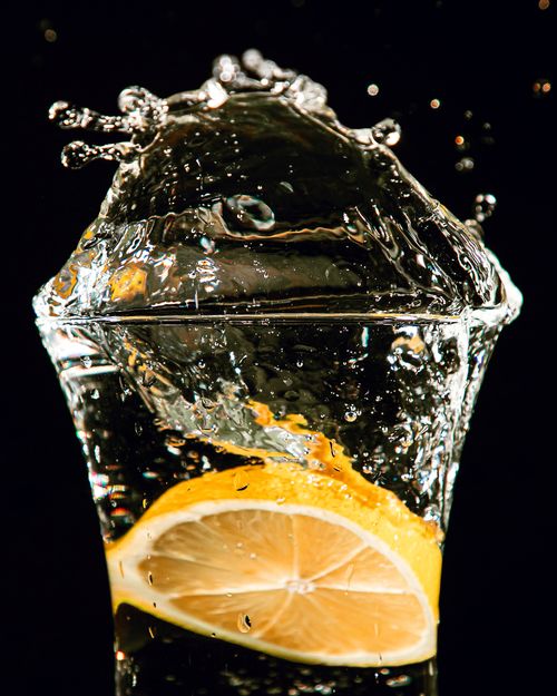 Free Vibrant splash of water over a lemon slice with a dramatic black backdrop. Stock Photo