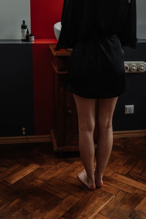 Free A woman stands barefoot on a wooden floor in a contemporary bathroom setting with a black skirt. Stock Photo