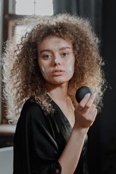 A young woman with curly hair applies skincare cream in her daily beauty routine.