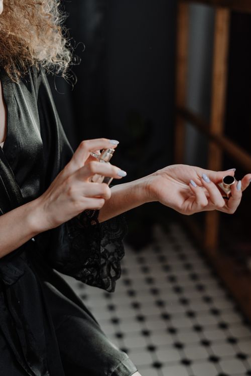Free Woman in a dark silk robe delicately applying perfume to her wrist indoors. Stock Photo