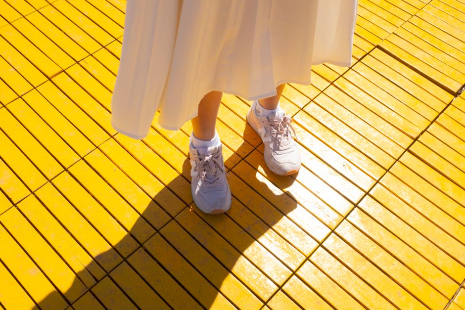White sneakers paired with a flowing skirt on a bright yellow wooden floor in vibrant sunlight.