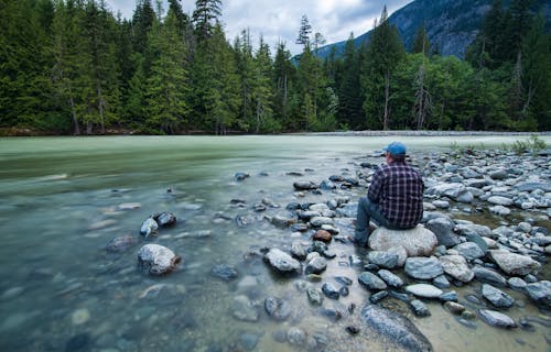 Человек, сидящий на камне возле водоема