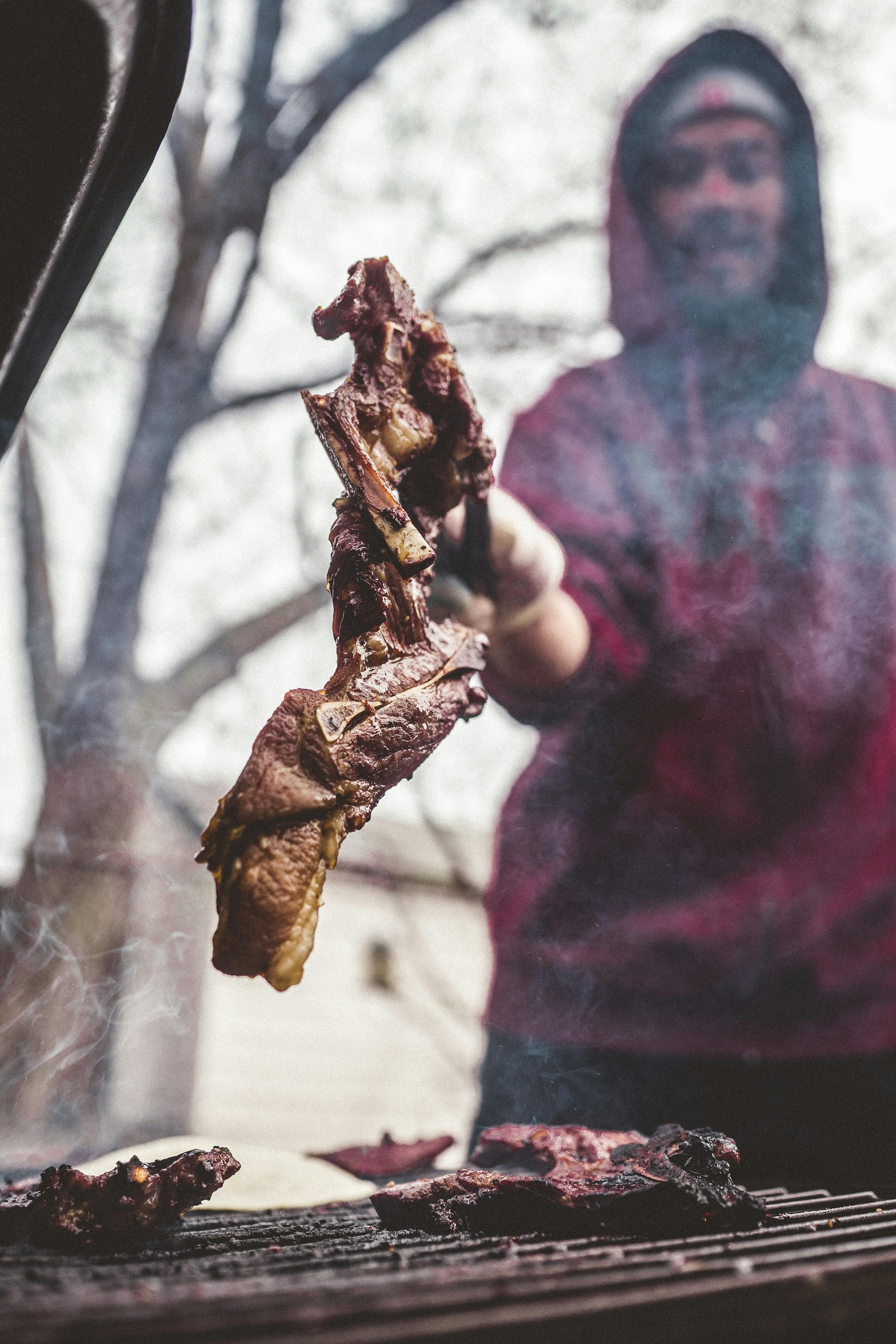 Man grilling meat outdoors on a barbecue, depicting a casual cooking vibe.