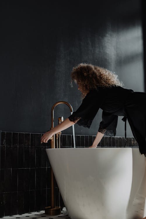 Woman in Black Long Sleeve Shirt and Blue Denim Jeans Standing on Bathtub