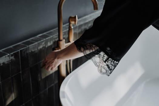 Close-up of a feminine hand reaching for a brass faucet in an elegant bathroom setting.