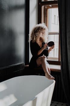 Young woman with curly hair in a stylish bathroom enjoying a beauty routine.