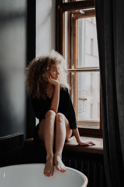 Free Woman in Black Tank Top Sitting on Window Stock Photo