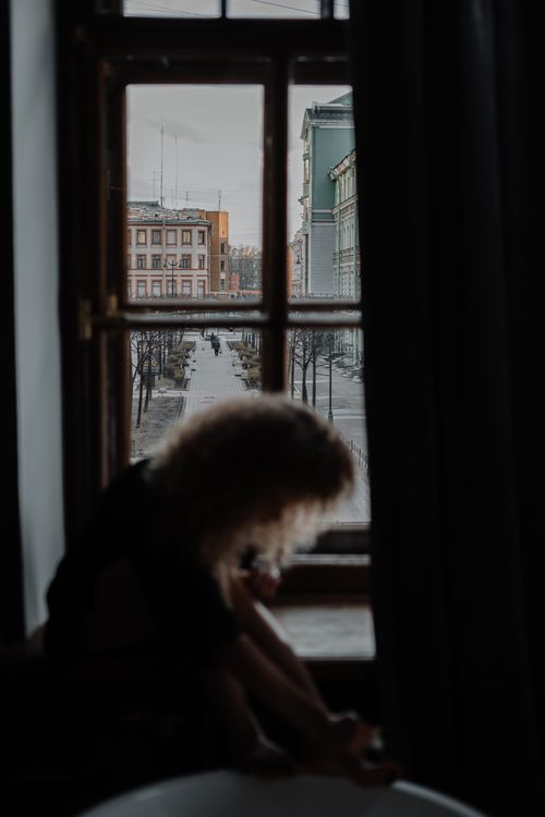 Free Silhouette of a woman sitting by a window, overlooking a historic city street. Stock Photo