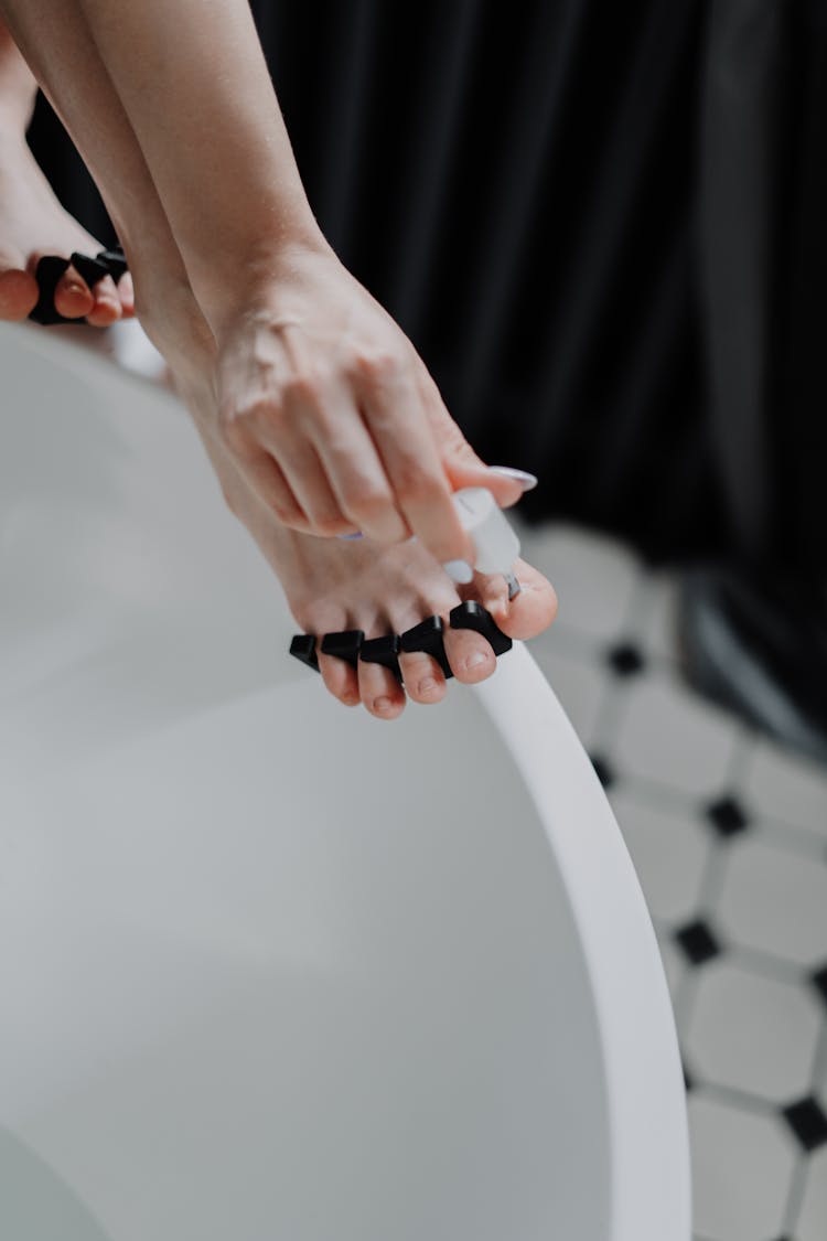 A Woman Applying Nail Polish On Her Toenails