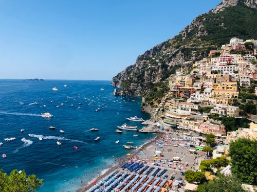 Free Scenic view of Amalfi Coast settlement located on green cliff near picturesque blue sea with floating boats on sunny summer day Stock Photo