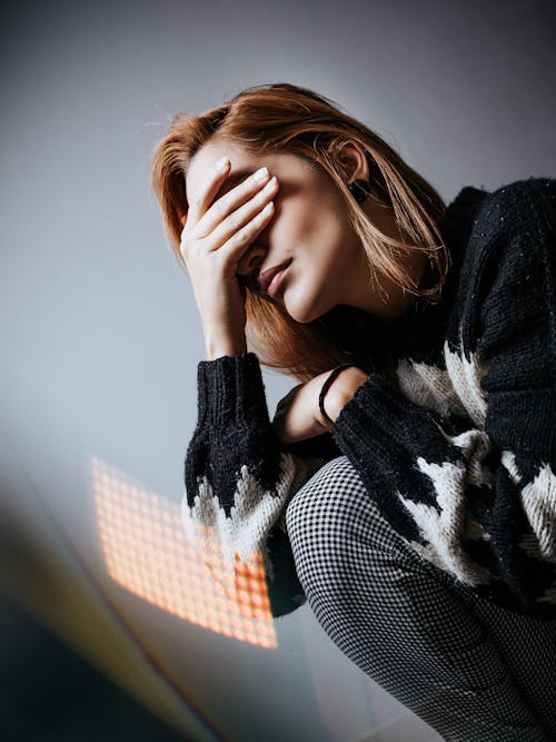 Free Unhappy depressed female sitting on floor against wall and huffing knee while covering eyes with hand in despair Stock Photo