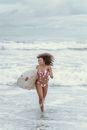 Positive sporty black female surfer with surfboard running on beach