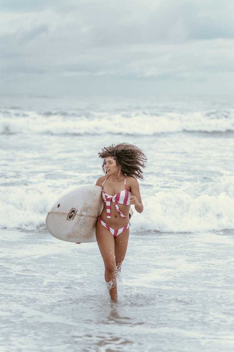 Positive Sporty Black Female Surfer With Surfboard Running On Beach