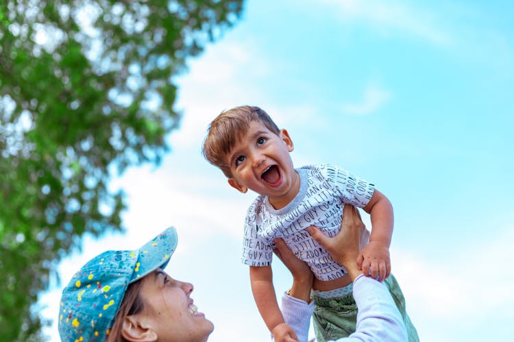 A Woman In A Blue Cap Lifting A Boy