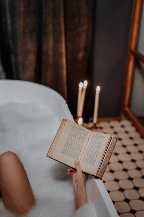 Free Person Reading Book on White Bathtub Stock Photo