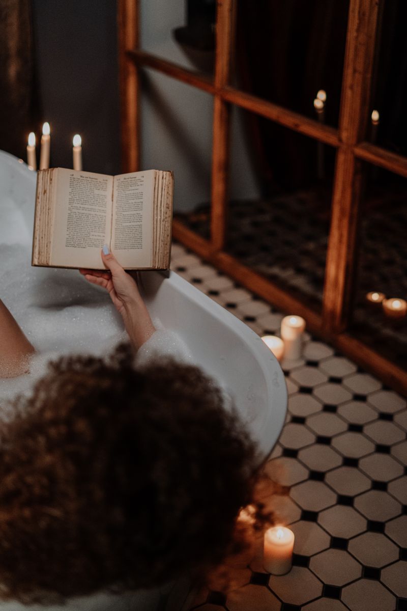 Person relaxing in bath reading a book for self-care