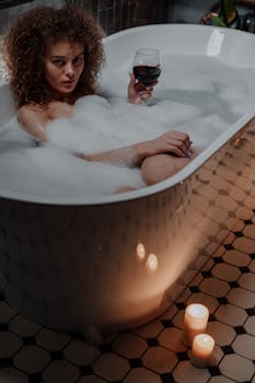 一位女士在泡泡浴中手持一杯葡萄酒，周围点着蜡烛，营造出平静的氛围
