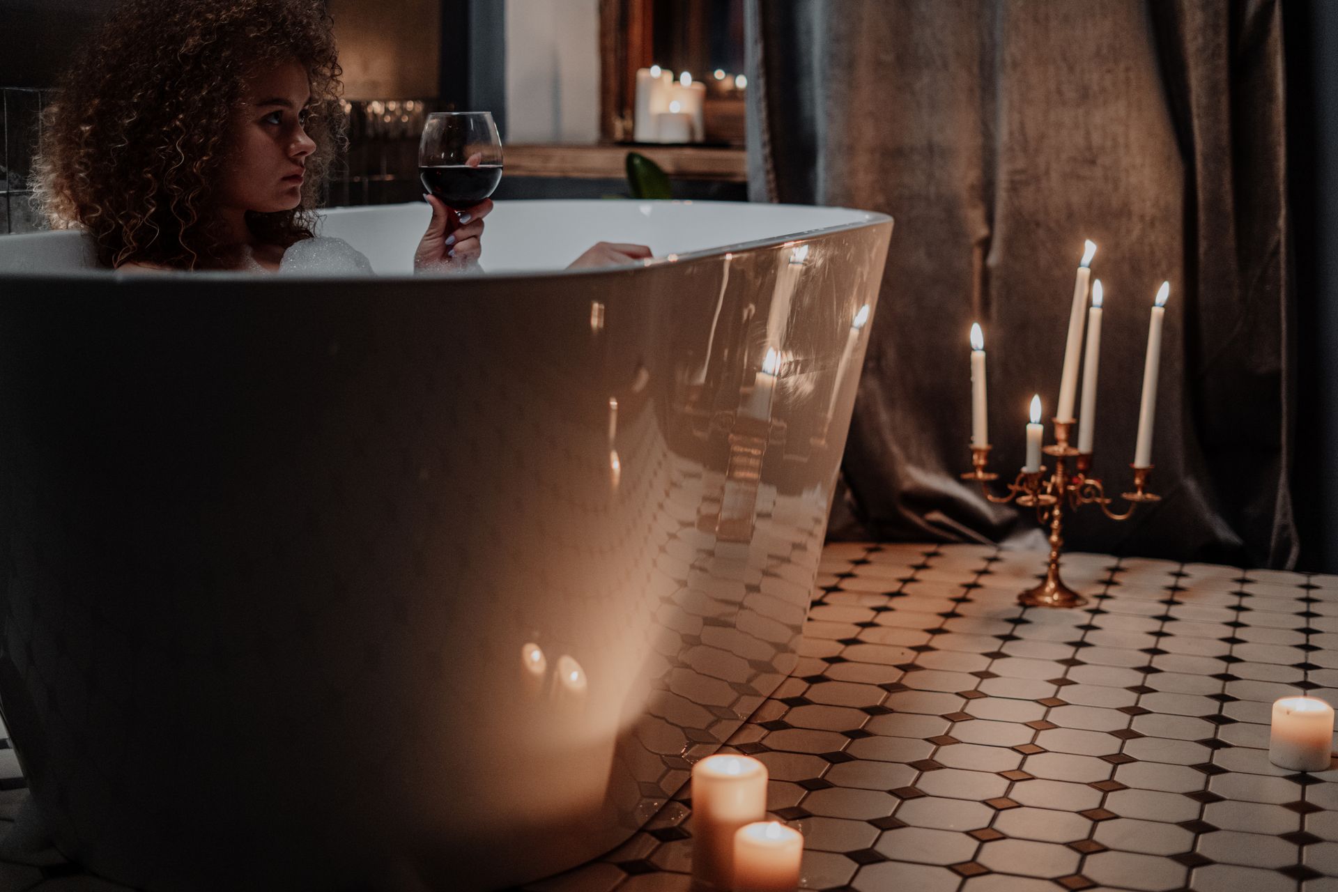 Woman relaxing in a candlelit bath enjoying a glass of wine.
