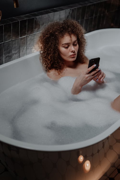 Free Woman in Bathtub Holding Black Smartphone Stock Photo