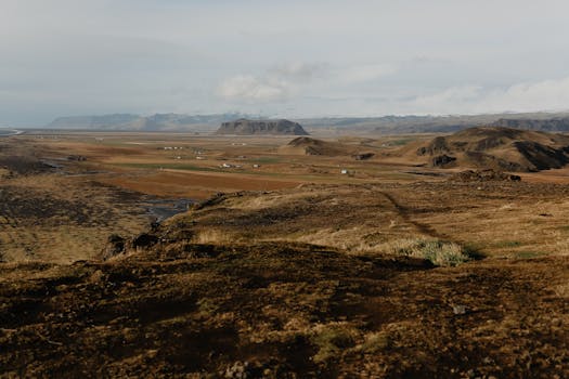 A broad view of a rocky landscape featuring distant mountains under a cloudy sky.