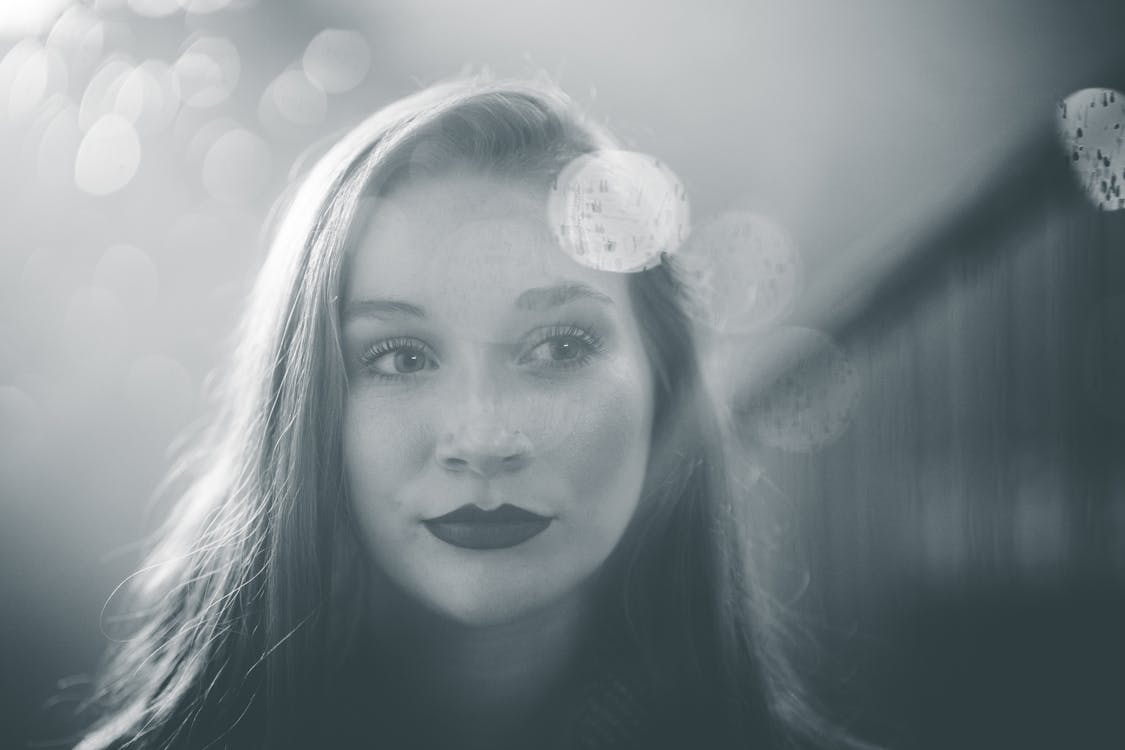 Black and white female with long hair and lipstick looking away while standing against blurred bokeh background