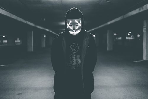 Free Black and white man in hooded wear standing on parking lot with scary neon mask on face Stock Photo