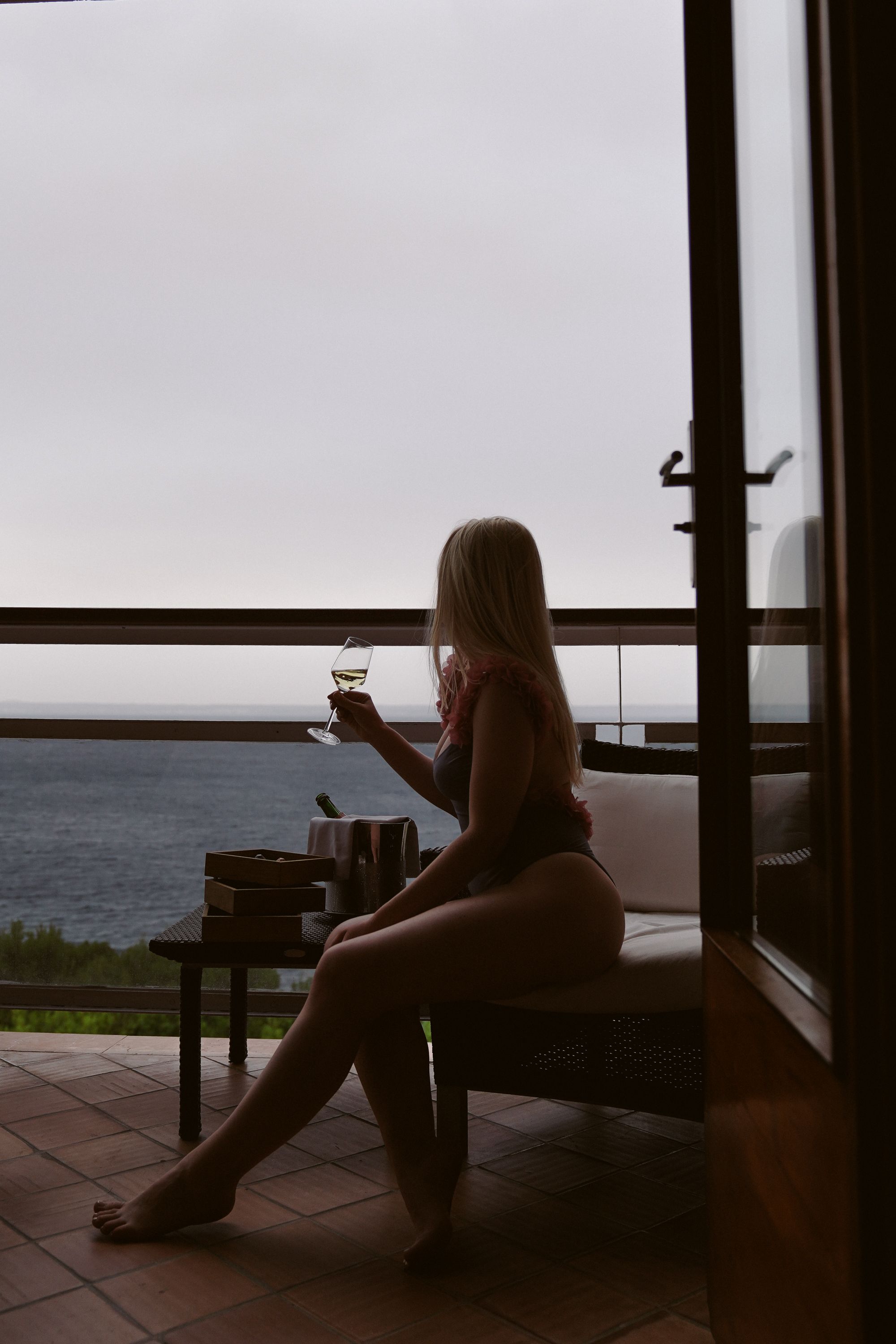 Elegant woman in swimwear enjoys wine and ocean view from balcony.