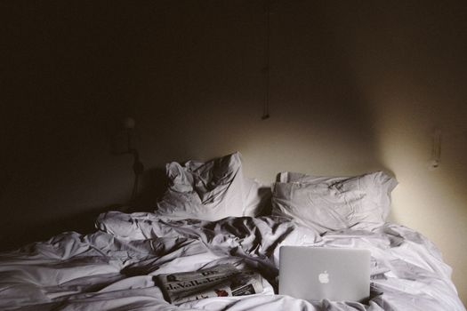 A tranquil bedroom scene featuring white bedding, a laptop, and a newspaper on the bed.