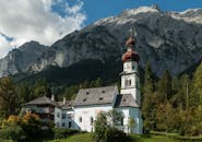 这座风景如画的教堂坐落在阿尔卑斯山，背靠令人惊叹的山脉，四周环绕着郁郁葱葱的绿色环境