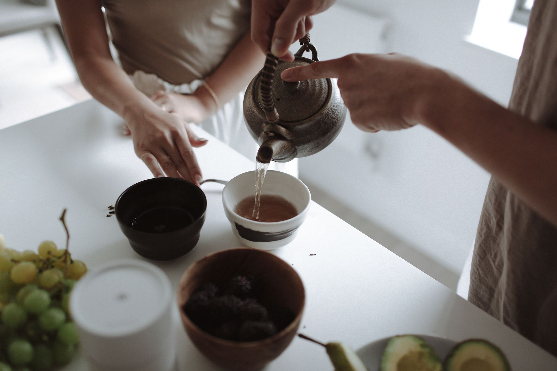 Close-up of tea being poured into a cup with fruit on the table, creating a cozy indoor scene.