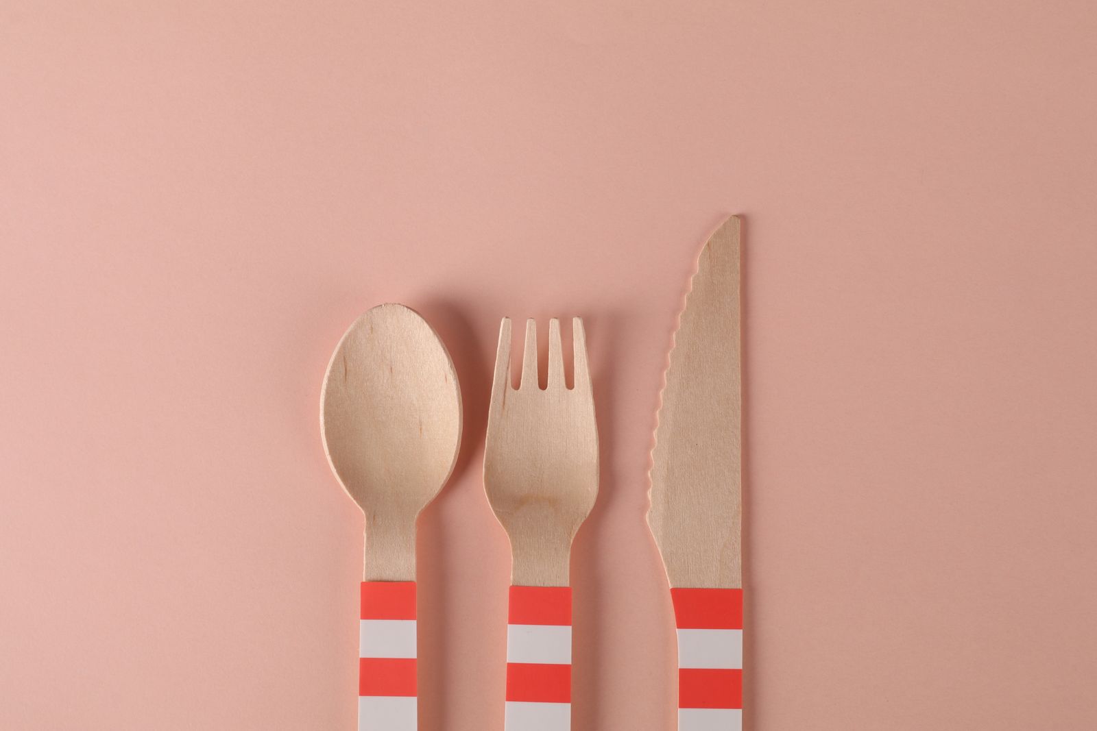 Minimalist arrangement of eco-friendly wooden utensils on a pastel pink background.