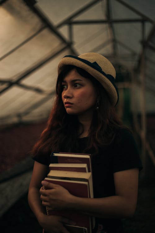 Close-Up Shot of a Pretty Woman in Black Shirt with Sun Hat Holding Books