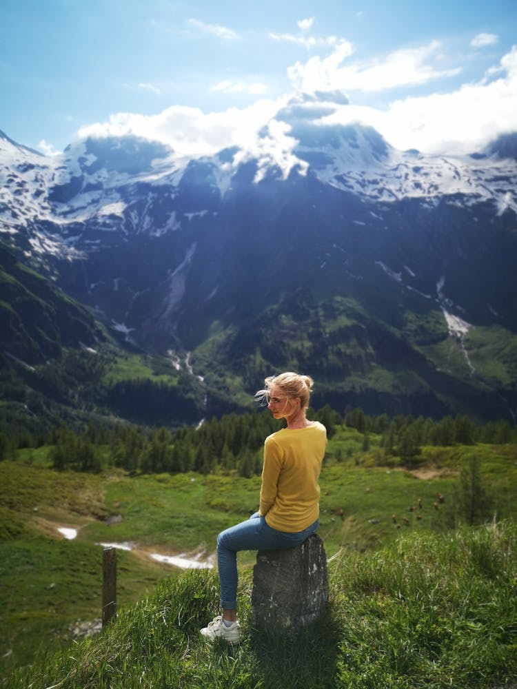 A Woman Sitting On A Rock Overlooking The Mountain Scenery