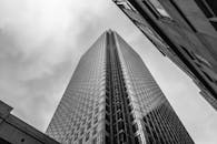 从低角度仰望现代摩天大楼，玻璃窗映照着阴沉的天空