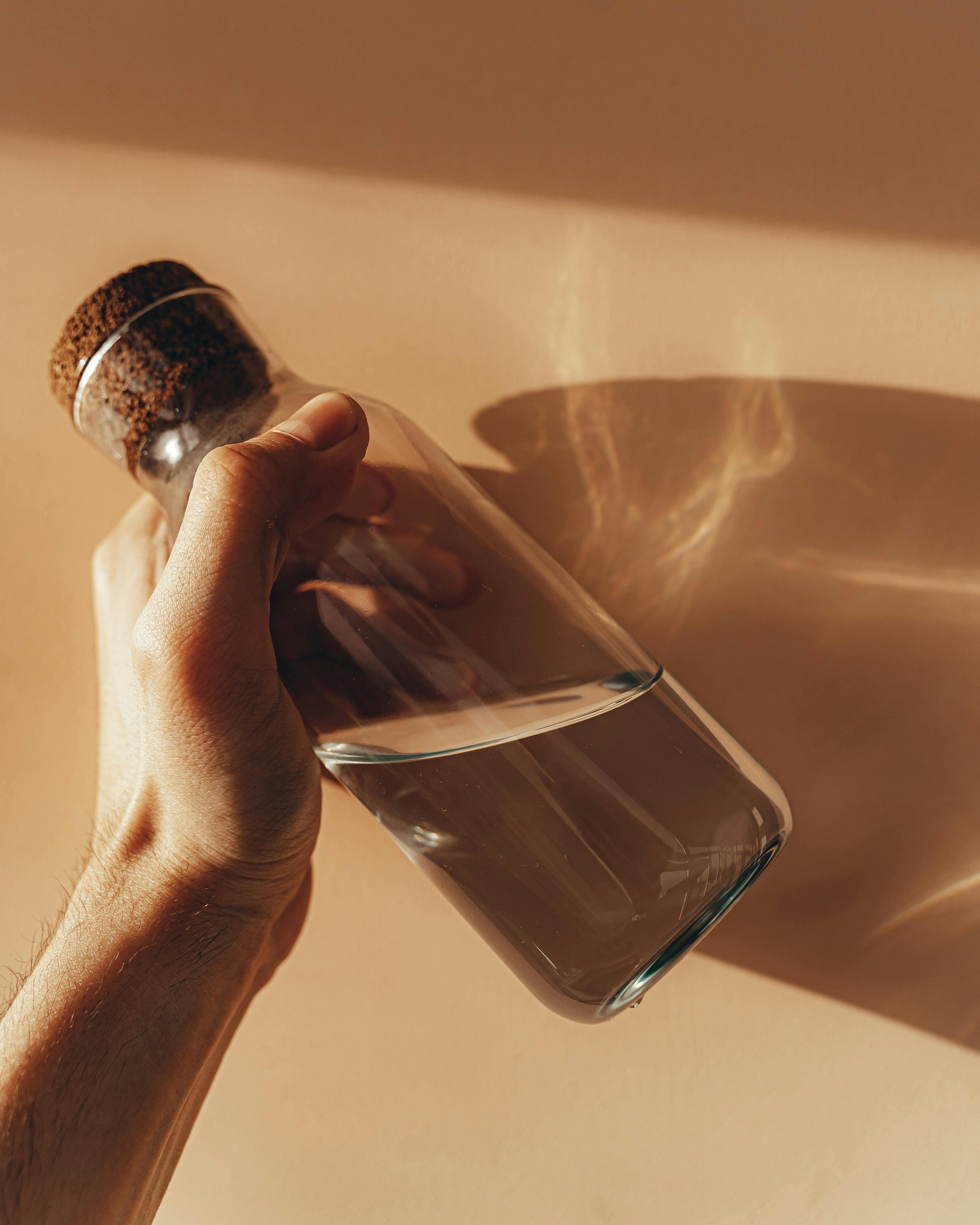 glass water bottle in hand of faceless man near wall