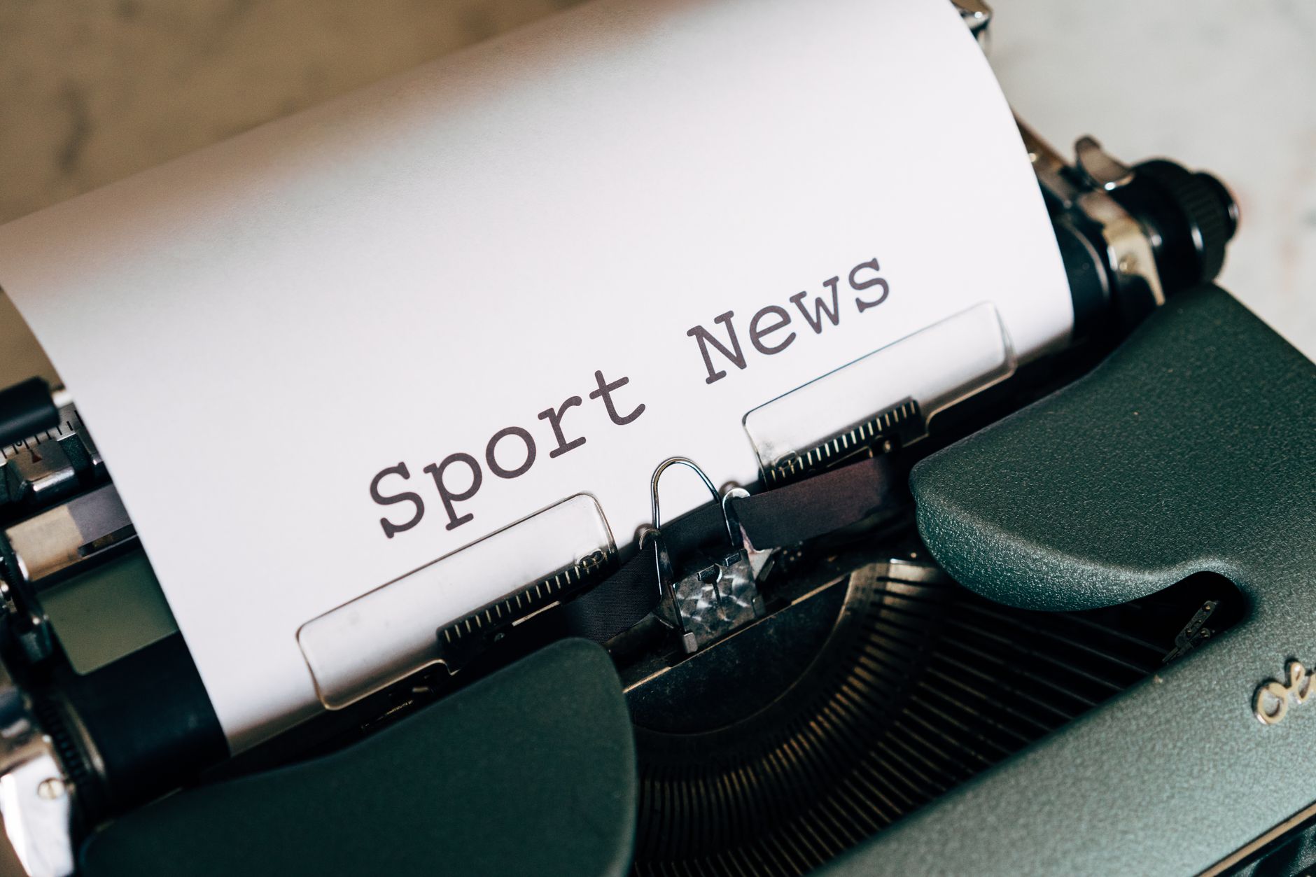 Close-up of a vintage typewriter with 'Sport News' typed on paper, evoking retro charm.