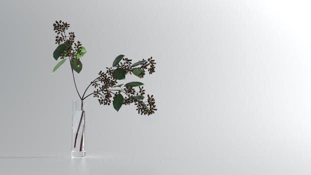 Branch of delicate lilac flower with small buds and green leaves placed in glass vase against white background