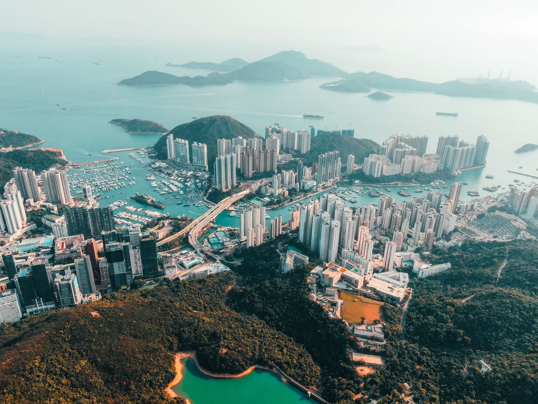 Amazing drone view of modern city with contemporary skyscrapers and harbor on sea shore with green hills and small islands