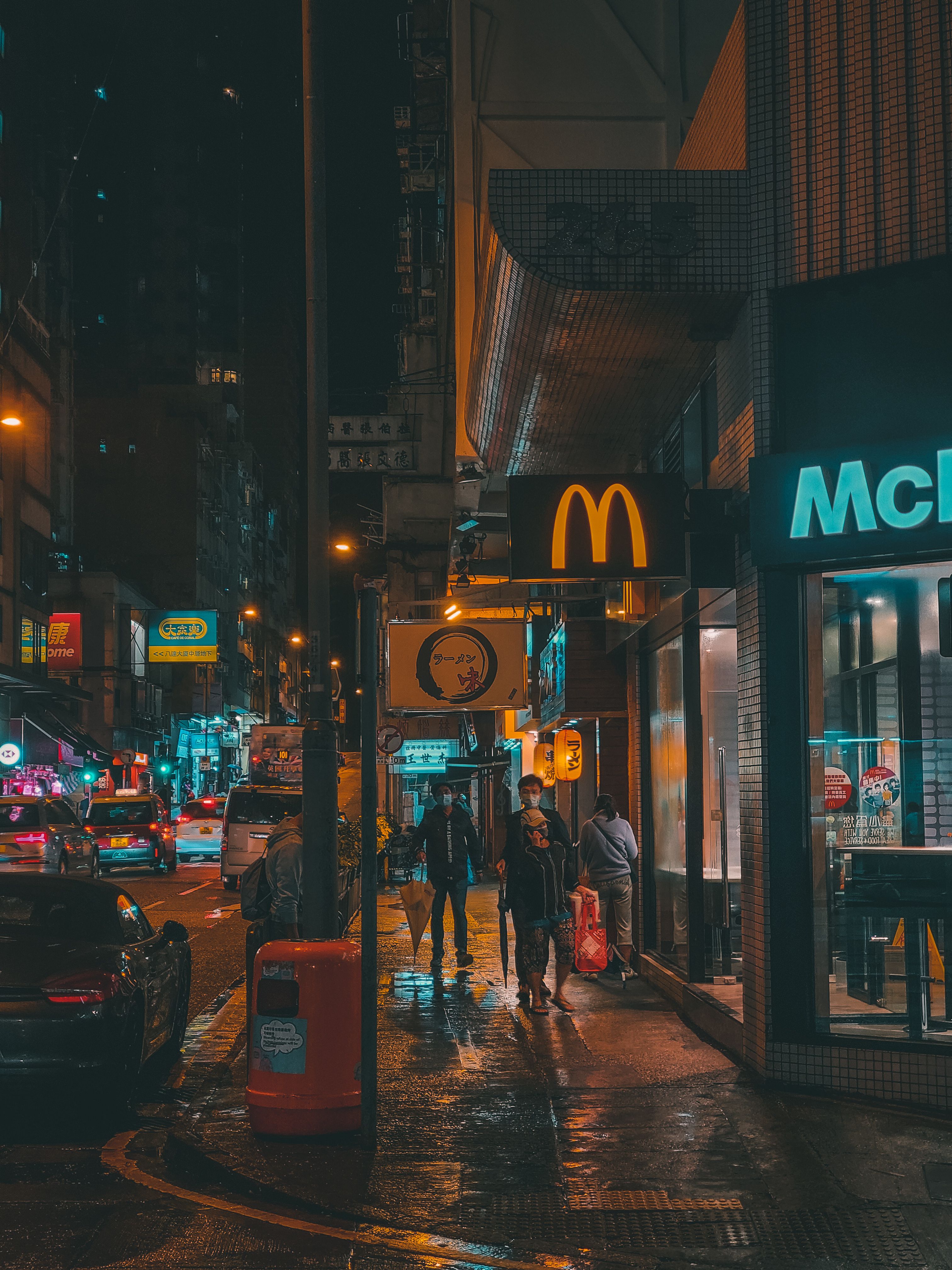 雨夜，一位匿名人士走在市中心灯火通明的商店和餐厅附近的街道上
