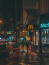 雨夜，一位匿名人士走在市中心灯火通明的商店和餐厅附近的街道上